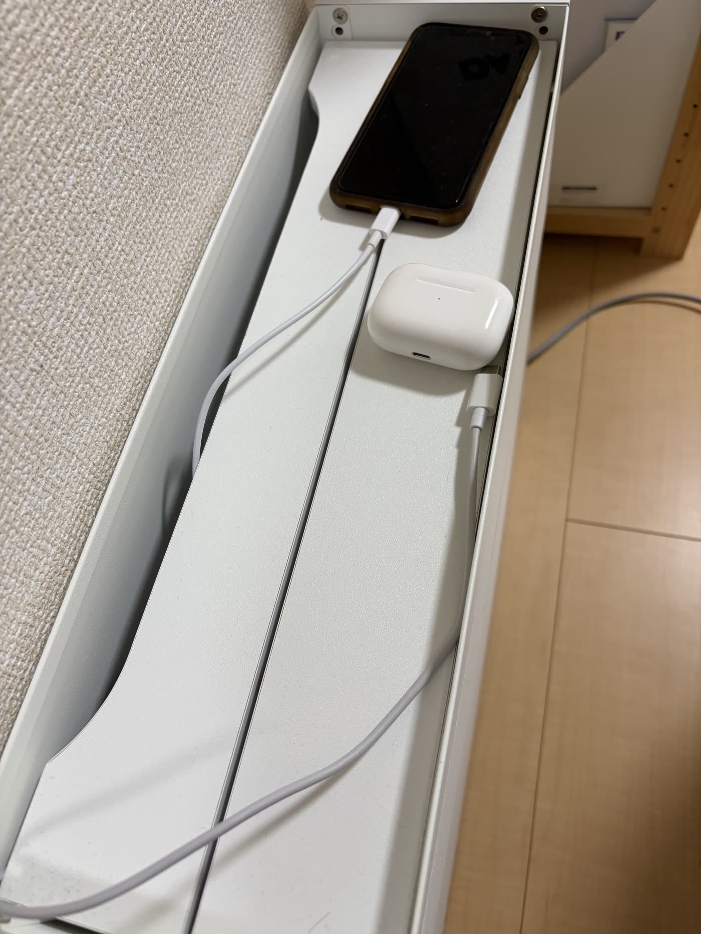 収納ボックスの天板を開けた内部。ケーブルを中に通してスマホとAirPodsを充電している